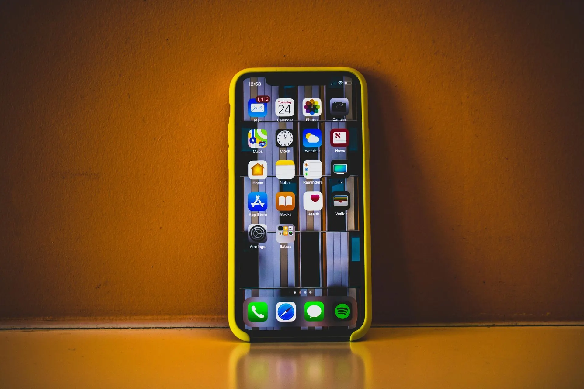Ein gelbes iPhone mit App-Symbolen lehnt an einer orangefarbenen Wand auf einer gelben Oberfläche.