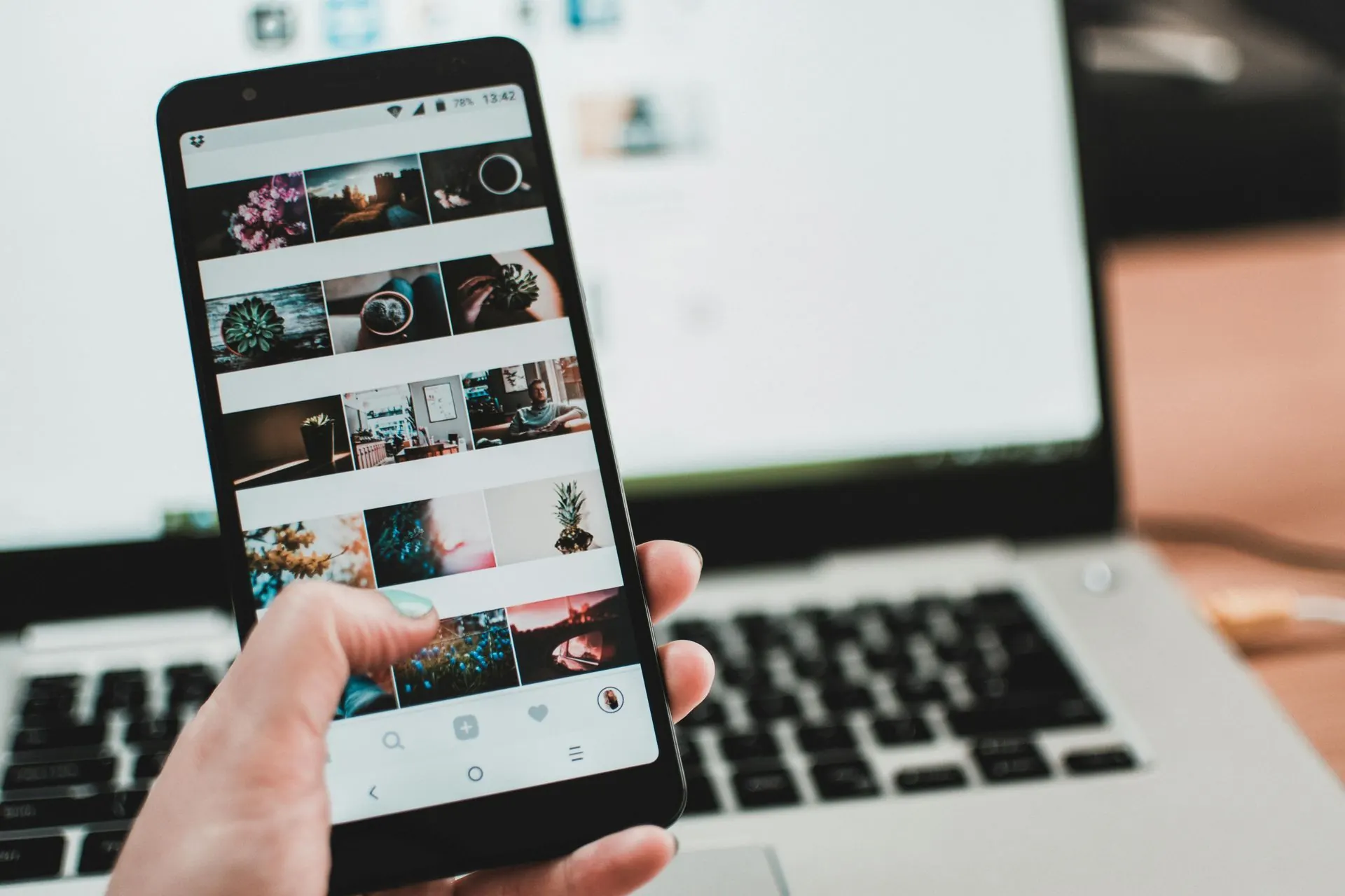 Eine Person hält ein Smartphone in der Hand, auf dem Fotos angezeigt werden, vor einem Laptop.