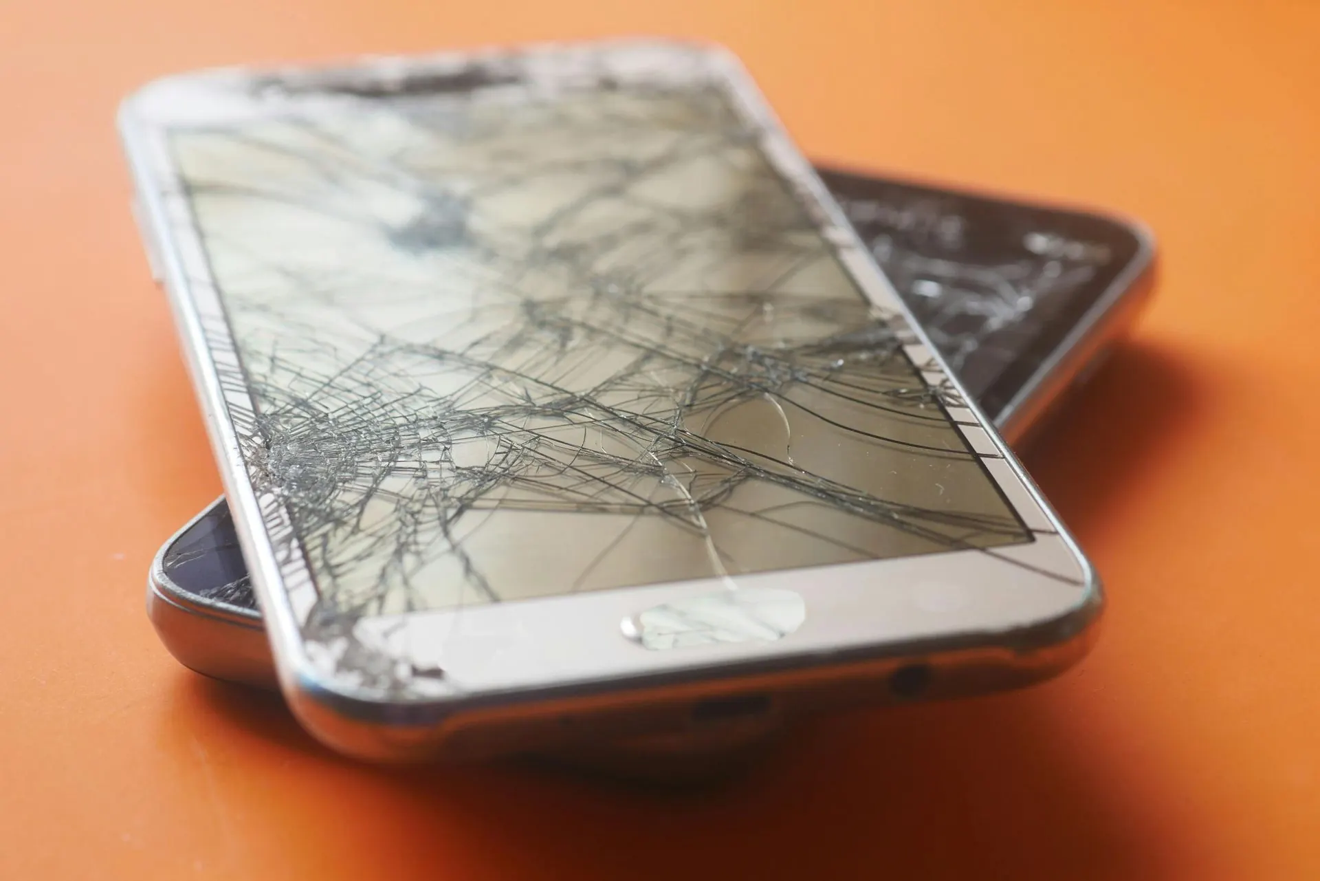 Zwei gesprungene Smartphones, eines übereinander, auf einer orangefarbenen Oberfläche.