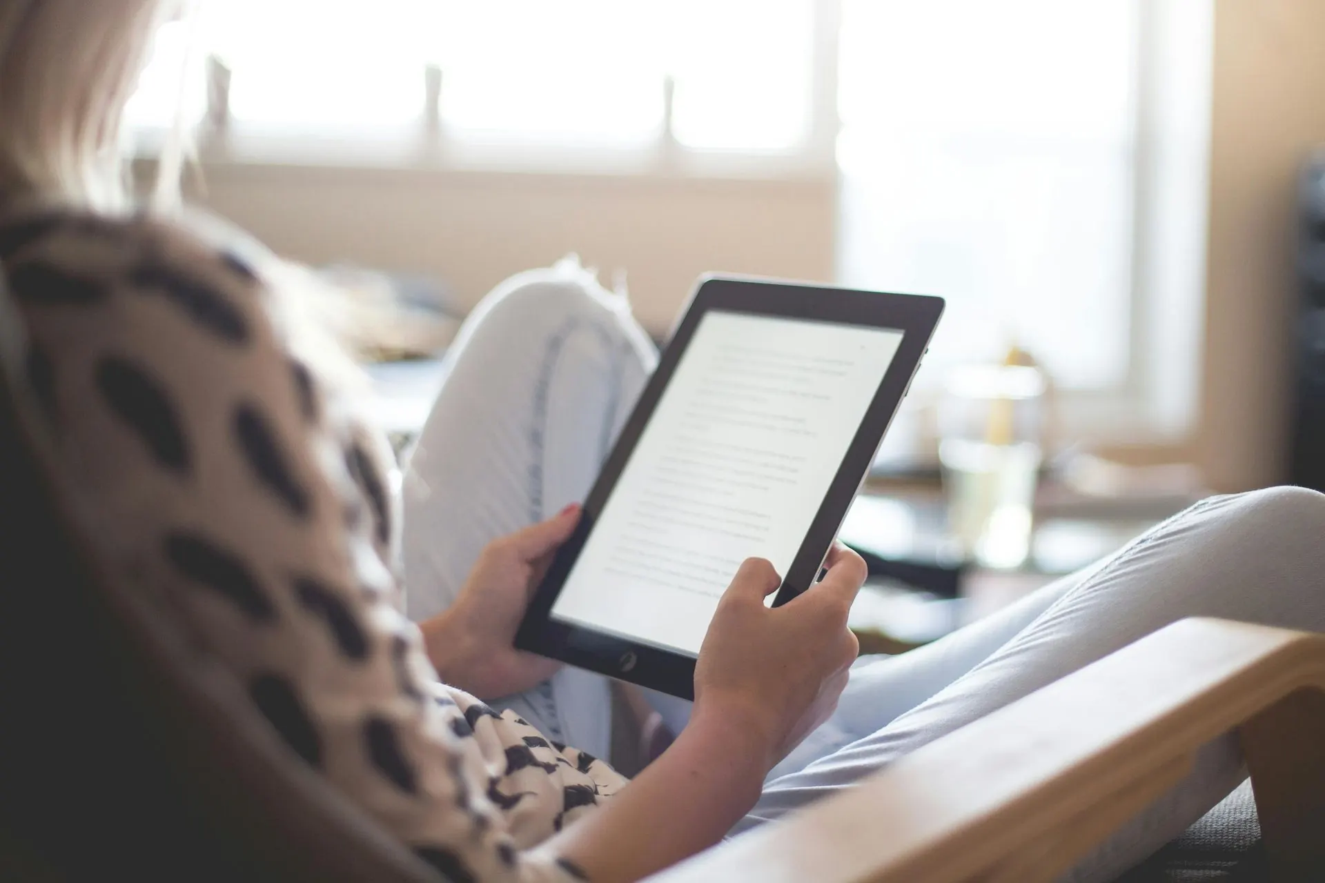 Frau sitzt und liest einen E-Reader. Innenbereich, natürliches Licht.