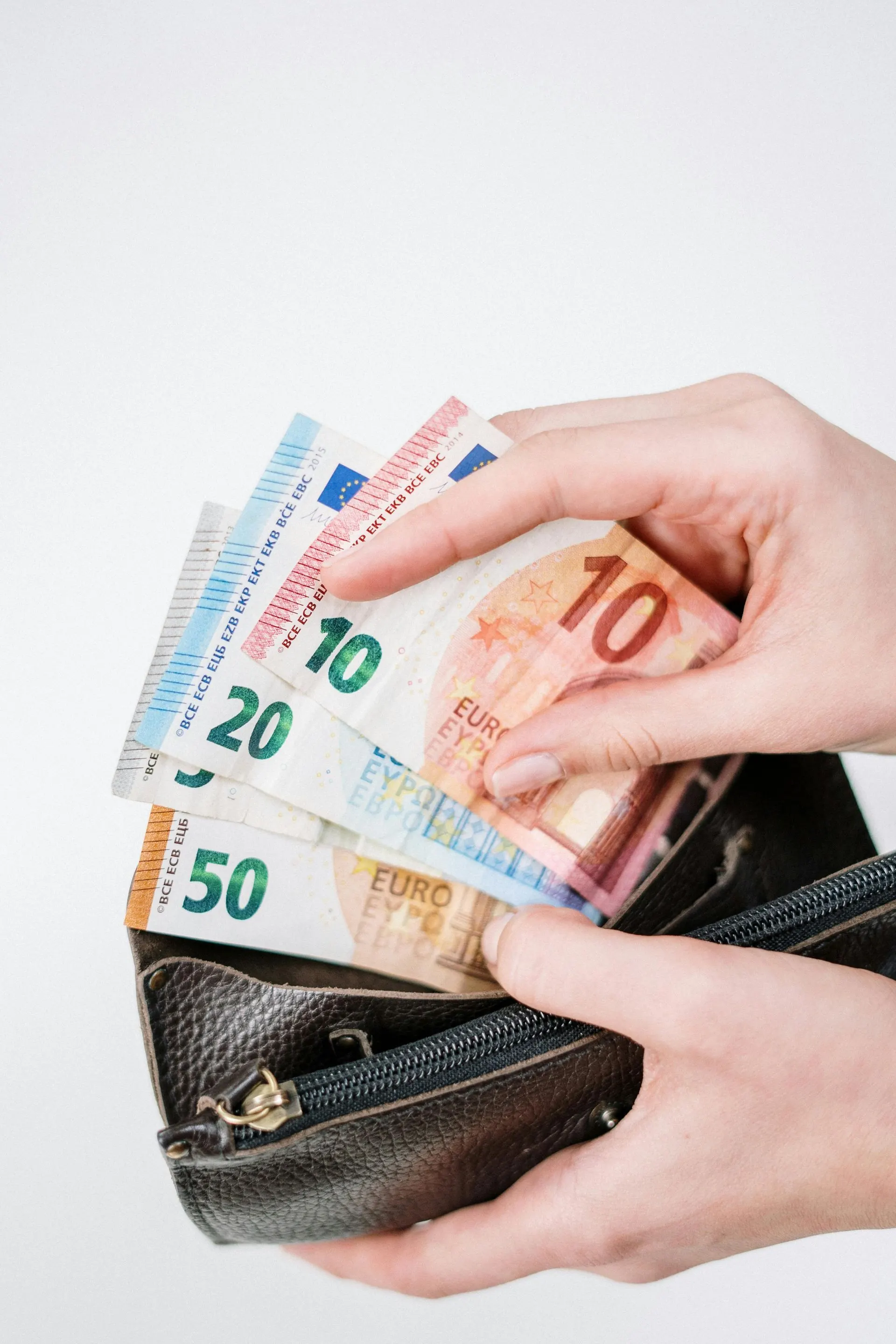 Hände halten Euro-Banknoten aus einem Portemonnaie: 50, 20, zwei 10er, vor weißem Hintergrund.