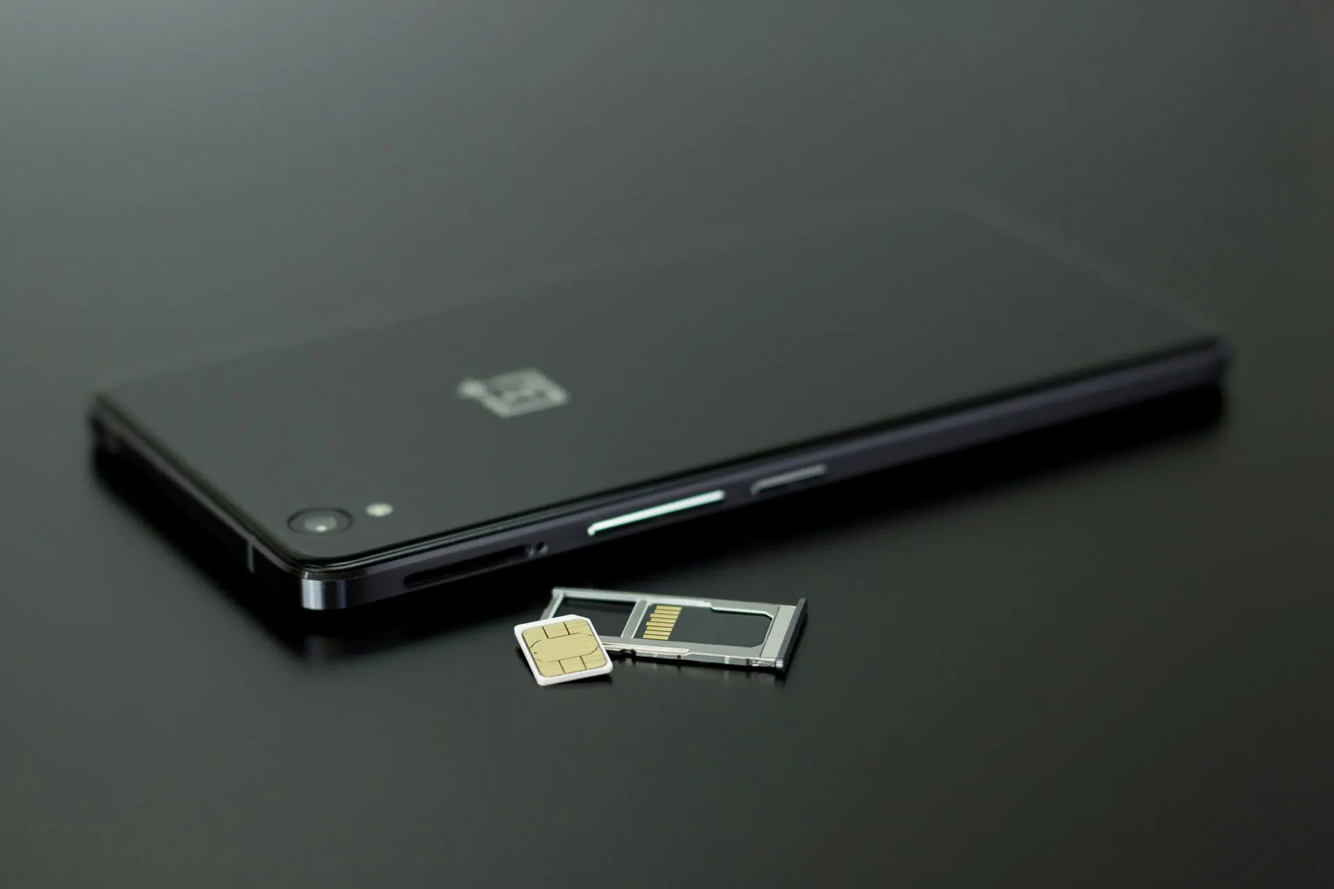 Schwarzes Smartphone mit SIM-Kartenfach und SIM-Karte auf dunkler Oberfläche.