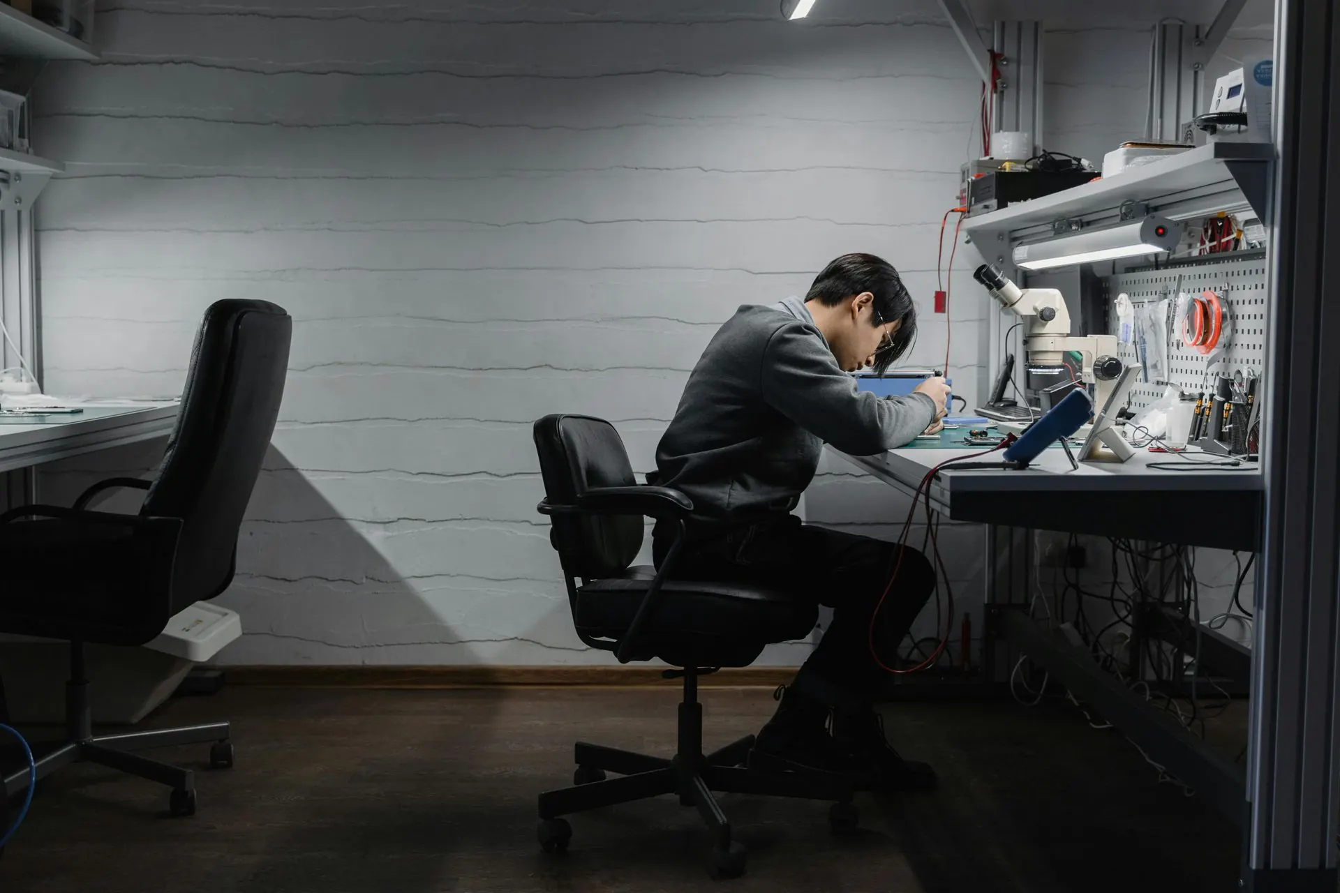 Eine Person arbeitet an einer Werkbank in einem schwach beleuchteten Raum an Elektronikgeräten.
