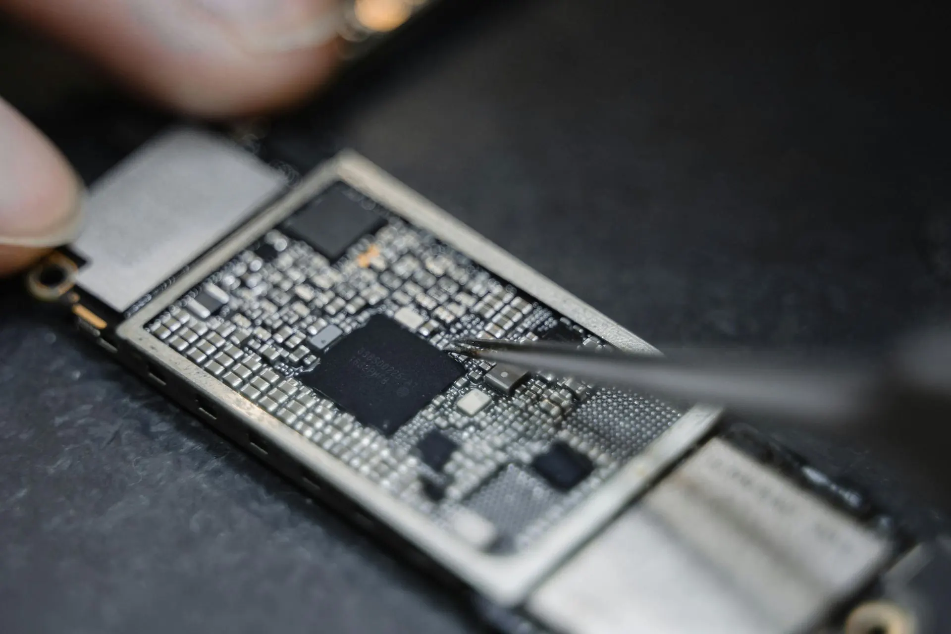 Nahaufnahme einer Leiterplatte, auf der eine Person mit einer Pinzette einen Chip manipuliert.