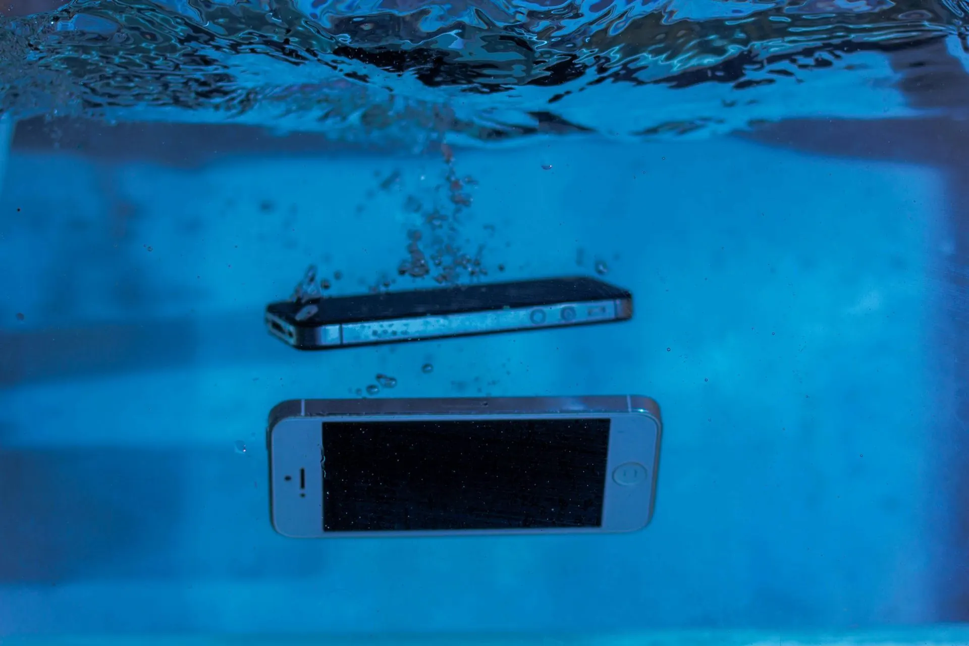 Zwei Smartphones, die in blauem Wasser untergetaucht sind, Blasen steigen auf.