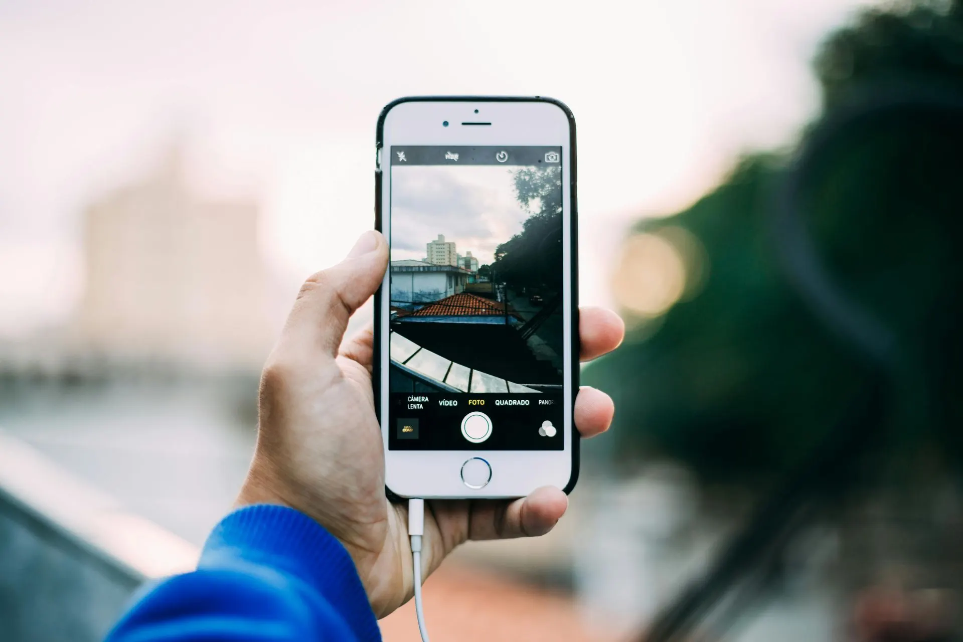 Eine Hand hält ein Smartphone und fotografiert im Freien ein Gebäude.